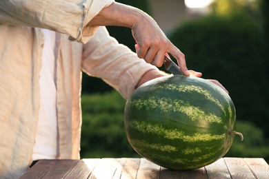 Man cutting tasty ripe watermelon at wooden table outdoors, closeup