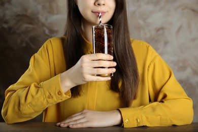 Photo of Woman drinking cola with ice at wooden table against grey background, closeup. Refreshing soda water