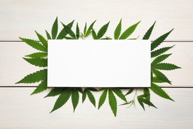 Fresh green hemp leaves and blank card on white wooden table, top view. Space for text