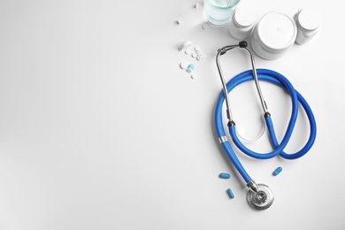 Stethoscope and pills on light background, top view. Medical equipment