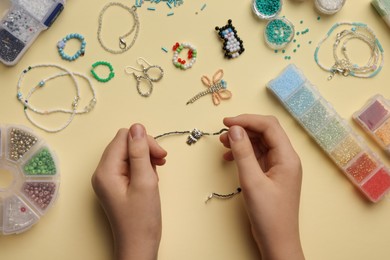 Girl making beaded jewelry on beige background, top view