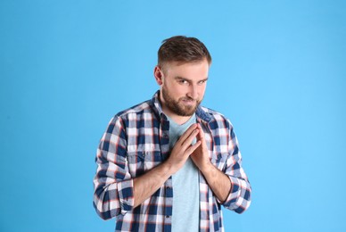 Greedy young man rubbing hands on light blue background