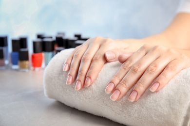 Young woman waiting for manicure near bottles of nail polish at table in salon, closeup. Space for text