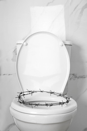 Toilet bowl with barbed wire near marble wall. Hemorrhoids concept