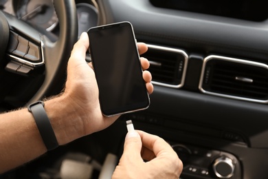 Man connecting charging cable to smartphone in car, closeup