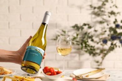 Woman holding bottle of wine over table with different snacks, closeup