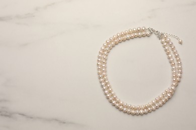 Photo of Beautiful pearl necklace on white marble table, top view. Space for text