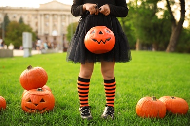 Little girl with pumpkin candy bucket wearing Halloween costume in park, closeup