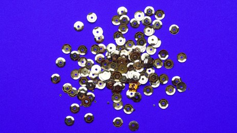 Photo of Pile of golden sequins on blue background, top view
