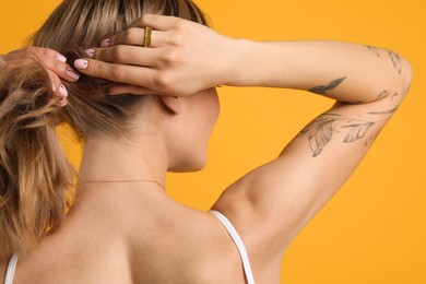 Beautiful woman with tattoos on body against yellow background, back view