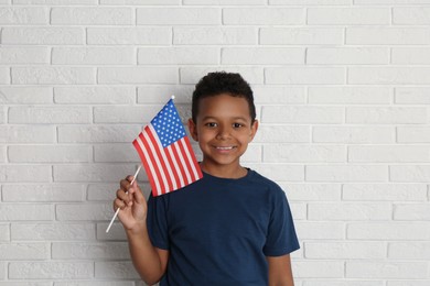 Happy African-American boy holding national flag near white brick wall