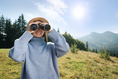 Photo of Young woman with binoculars in mountains on sunny day, space for text