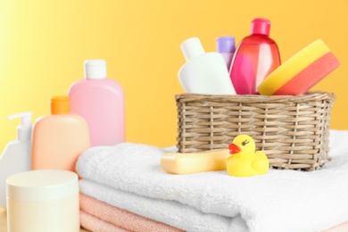 Wicker basket with baby cosmetic products, toy and towels against color background, closeup