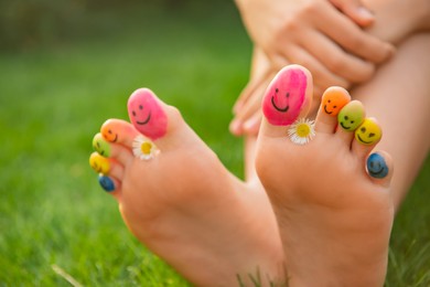 Teenage girl with chamomiles and smiling faces drawn on toes outdoors, closeup