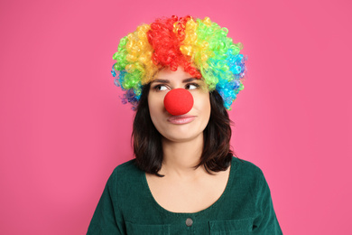 Emotional woman with rainbow wig and clown nose on pink background. April fool's day
