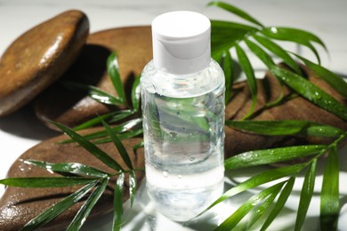 Bottle of micellar cleansing water, green twigs and spa stones on white table, closeup