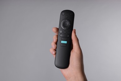 Photo of Woman holding TV remote control on grey background, closeup
