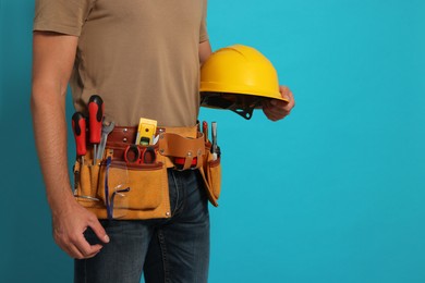 Professional builder with hard hat and tool belt on light blue background, closeup. Space for text