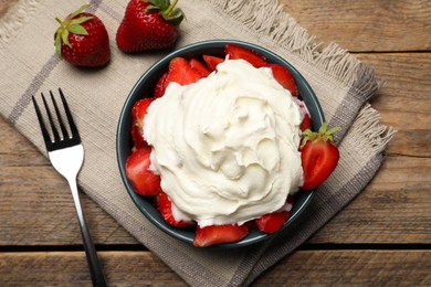 Bowl with delicious strawberries and whipped cream served on wooden table, flat lay