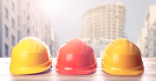 Hard hats on wooden surface at construction site with unfinished building. Banner design