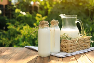 Bottles and jug of tasty fresh milk on wooden table outdoors, space for text