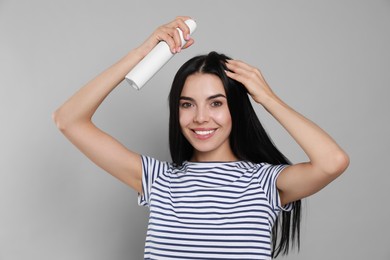 Woman applying dry shampoo onto her hair on light grey background