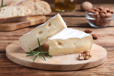 Tasty cut brie cheese with rosemary and walnut on wooden table
