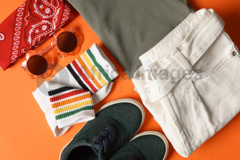 Stylish child clothes, shoes and accessories on orange background, flat lay