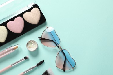 Set of makeup products and sunglasses on light blue background, flat lay. Space for text