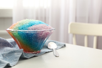Rainbow shaving ice in glass dessert bowl and spoon on white table indoors