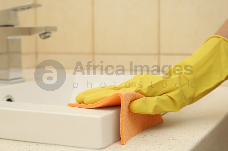 Woman cleaning sink with rag in bathroom, closeup