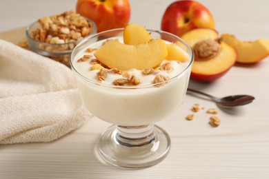 Tasty peach yogurt with granola and pieces of fruit in dessert bowl on white wooden table