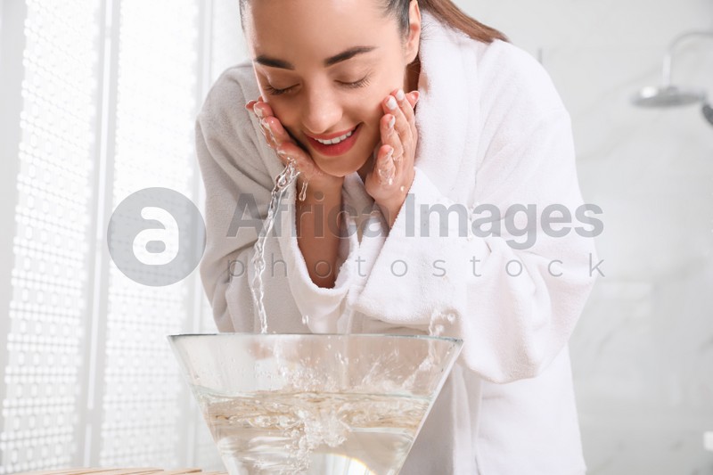 Beautiful young woman washing her face with water in bathroom