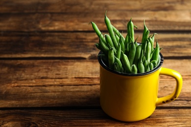Fresh green beans in mug on wooden table, space for text