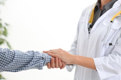 Doctor holding elderly patient hand on light background, closeup