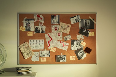 Detective board with fingerprints, crime scene photos and red threads on white wall in office