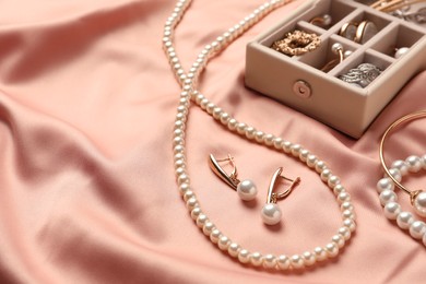 Photo of Box with luxurious pearl jewelry on pink silk, closeup