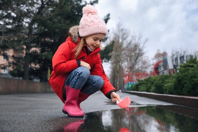 Little girl playing with paper boat near puddle outdoors