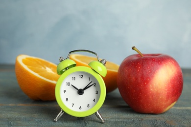Alarm clock, orange and apple on light blue wooden table. Meal timing concept
