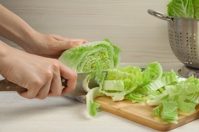 Woman cutting Chinese cabbage at white wooden kitchen table, closeup