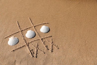 Playing Tic tac toe game with shells on sand, above view. Space for text
