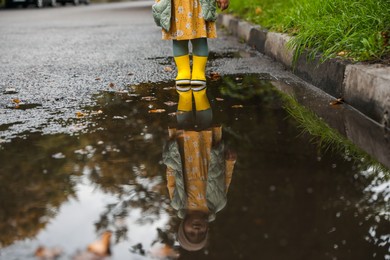 Little girl wearing yellow rubber boots standing in puddle outdoors, closeup