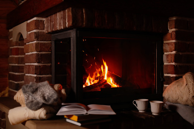 Knitwear and books near fireplace with burning wood indoors. Winter vacation
