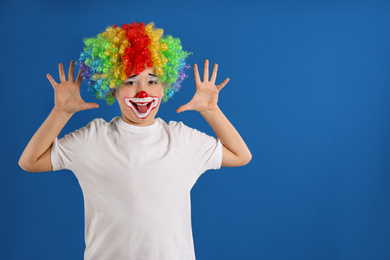 Preteen boy with clown makeup and wig on blue background, space for text. April fool's day