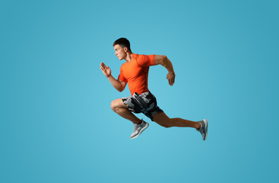 Athletic young man running on light blue background, side view