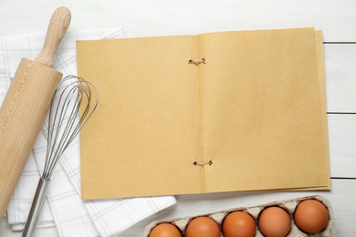 Photo of Blank recipe book, kitchen utensils and eggs on white wooden table, flat lay. Space for text
