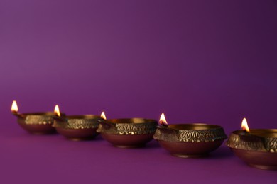 Photo of Lit diya lamps on purple background. Diwali celebration