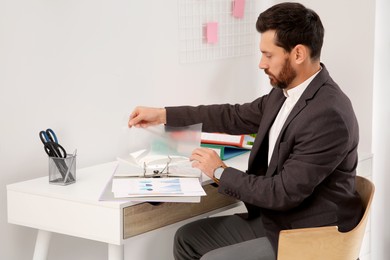 Photo of Businessman putting punched pocket into folder at white table in office