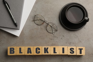 Wooden cubes with word Blacklist, cup of coffee and office stationery on grey table, flat lay