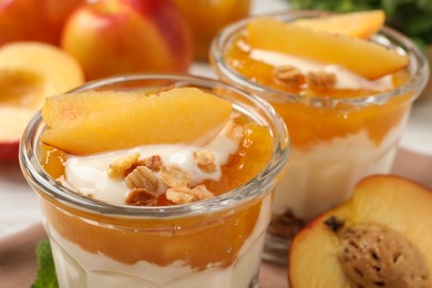 Tasty peach yogurt with granola, pieces of fruit and jam on table, closeup